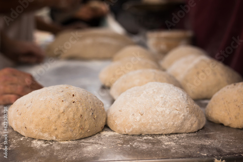 wheat dough shaped into loaves arranged in rows on the table before baking