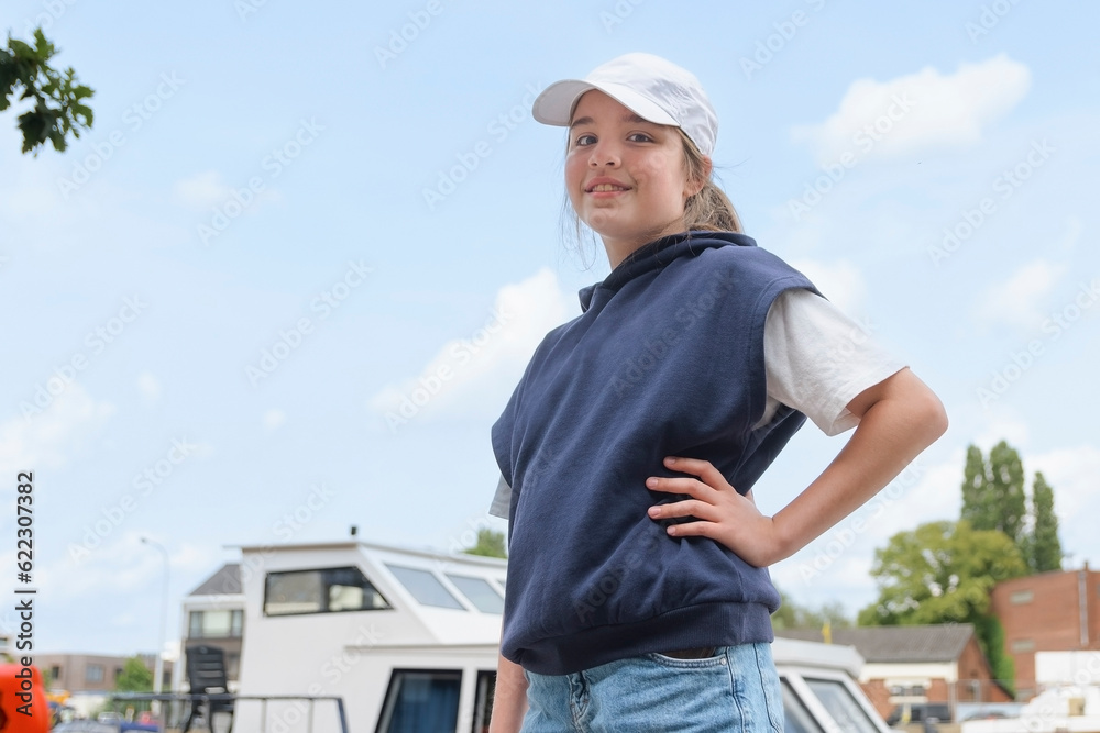 An embankment with yachts and a teenage girl. looks at camera. Baseball cap blue sweater. copy space