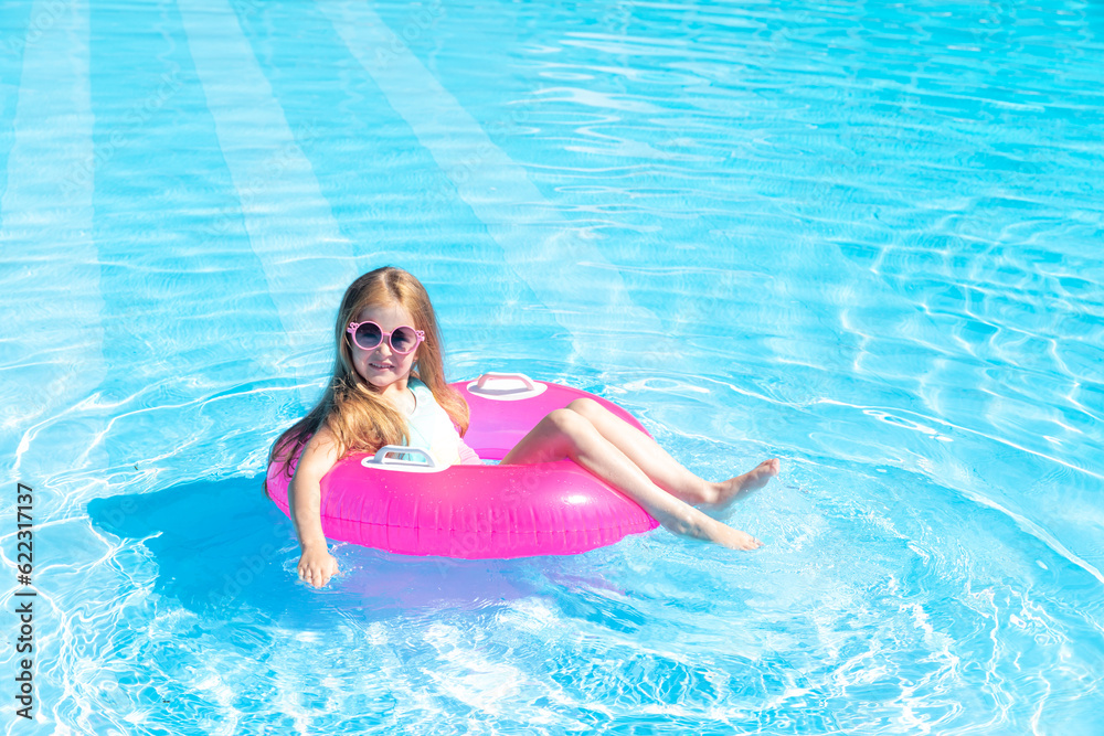 happy little girl swims in the pool in summer in sunglasses, space for text