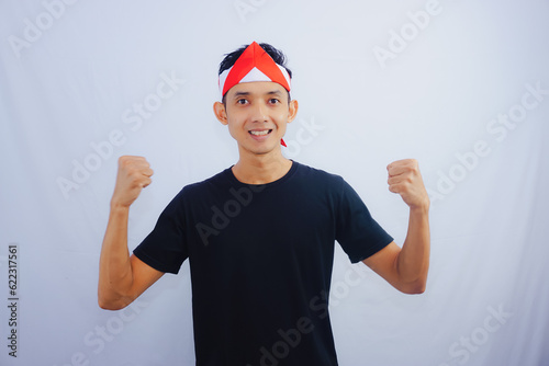 Young Asian man with indonesian flag clenched hand for celebrate Indonesia independence day on August 17, looking at camera with confident and excited expression isolated on white background