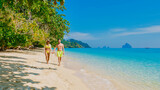 the backside of a couple of men and women sitting at the beach of Koh Kradan island in Thailand, during a vacation on a sunny day