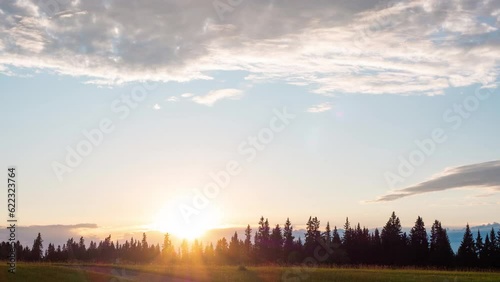 coloful sunset at pineforest 4k timelapse footage. Clouds traveling above wide angel view meadow landscape. Travel in nature in fall season amazing scenery. sun rays, sun burst over horizontal sky. photo