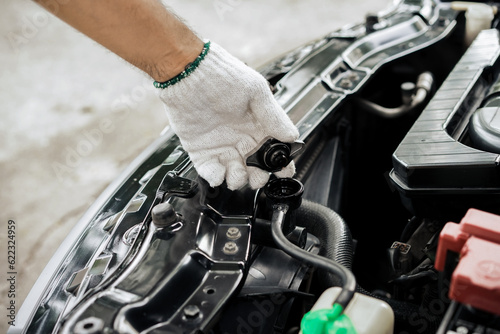 Close-up of hand of a gloved mechanic opening the radiator cap to check the coolant level. A man's hand is holding the radiator cap and opening it to check the water in the engine. car maintenance photo