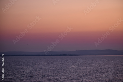 Fototapeta Naklejka Na Ścianę i Meble -  Sunrise sunset orange purple blue pink skies over ocean sea with mountains and beach on horizon line