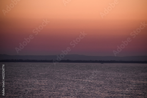 Sunrise sunset orange purple blue pink skies over ocean sea with mountains and beach on horizon line