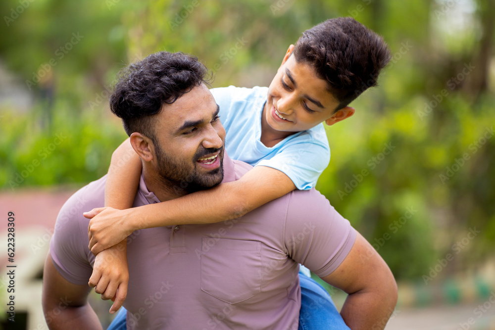 Joyful excited Indian father spining son by carrying on his piggy back at park - concept of childhood memories, weekend holidays and Carefree moments Joyful excited Indian father spining son by carrying on his piggy back at park - concept of childhood memories, weekend holidays and Carefree moments