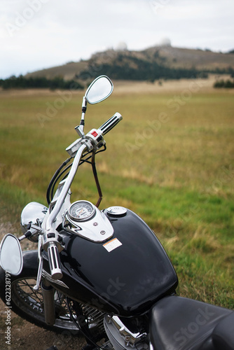 A black motorcycle stands by the side of a mountain road against the background of mountains and a field of mountains