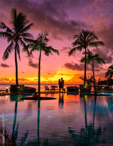 a couple of men and women watching the sunset on a tropical beach in Mauritius with palm trees by the swimming pool, Tropical sunset on the beach in Mauritius. © Fokke Baarssen
