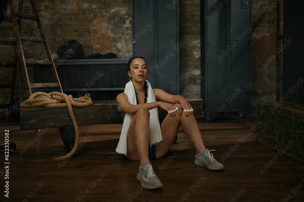 Woman boxer resting on bench with towel on neck Woman boxer resting on bench with towel on neck