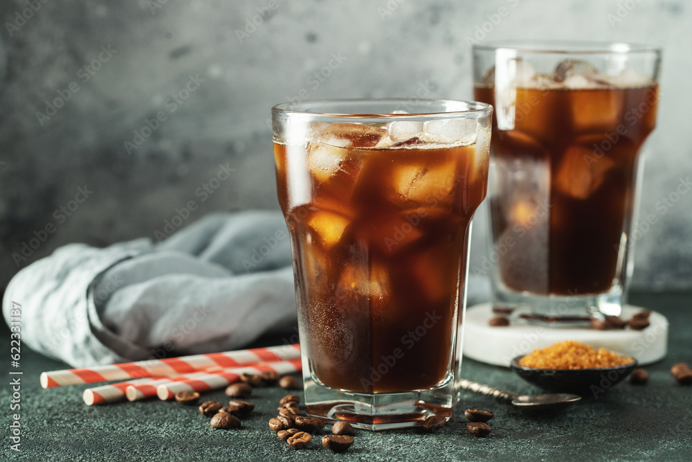Ice coffee in a tall glass with cream poured over, ice cubes and beans on a dark concrete table. Ice coffee in a tall glass with cream poured over, ice cubes and beans on a dark concrete table.