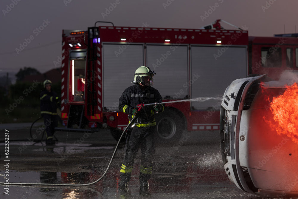 Fototapeta premium Firefighters fight the fire flame to control fire not to spreading out. Firefighter industrial and public safety concept. Traffic or car accident rescue and help action. 