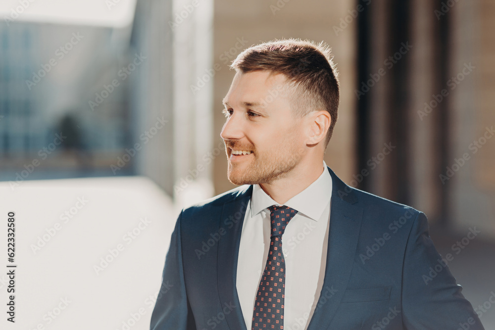 Sideways shot of cheerful unshaven male looks aside with joyful expression, wears formal clothes, being in good mood after successful meeting with business partners. People and work concept. Sideways shot of cheerful unshaven male looks aside with joyful expression, wears formal clothes, being in good mood after successful meeting with business partners. People and work concept.