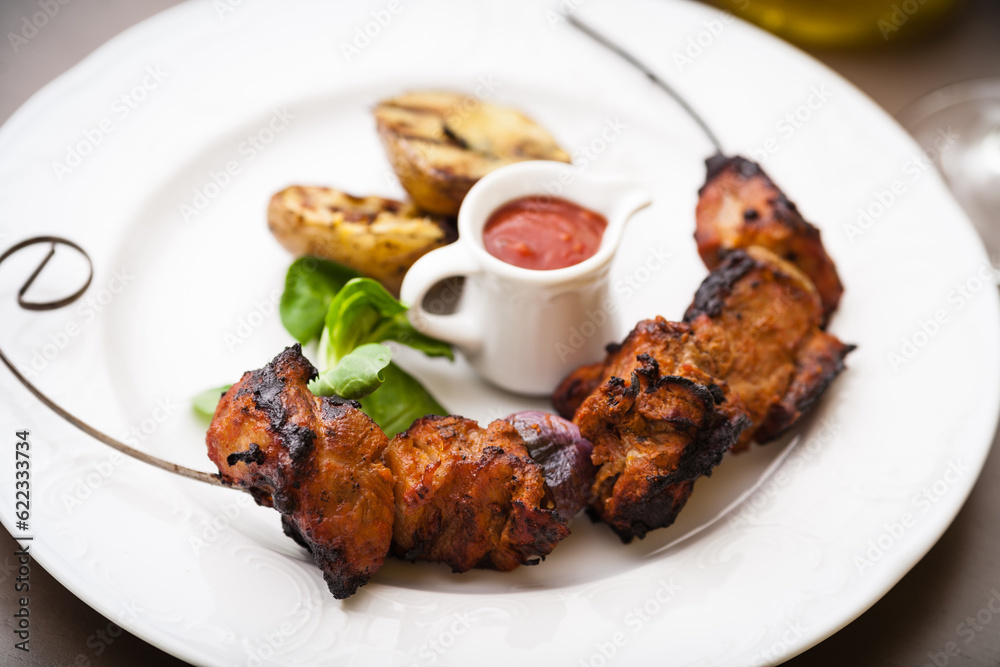 Pork shashlik with grilled potatoes served on a white plate Pork shashlik with grilled potatoes served on a white plate