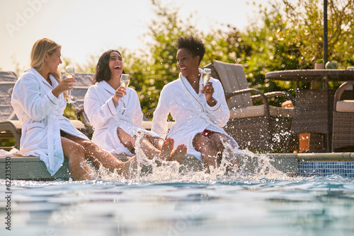 Group Of Mature Female Friends Wearing Robes Sitting With Feet In Pool Drinking Champagne On Spa Day photo