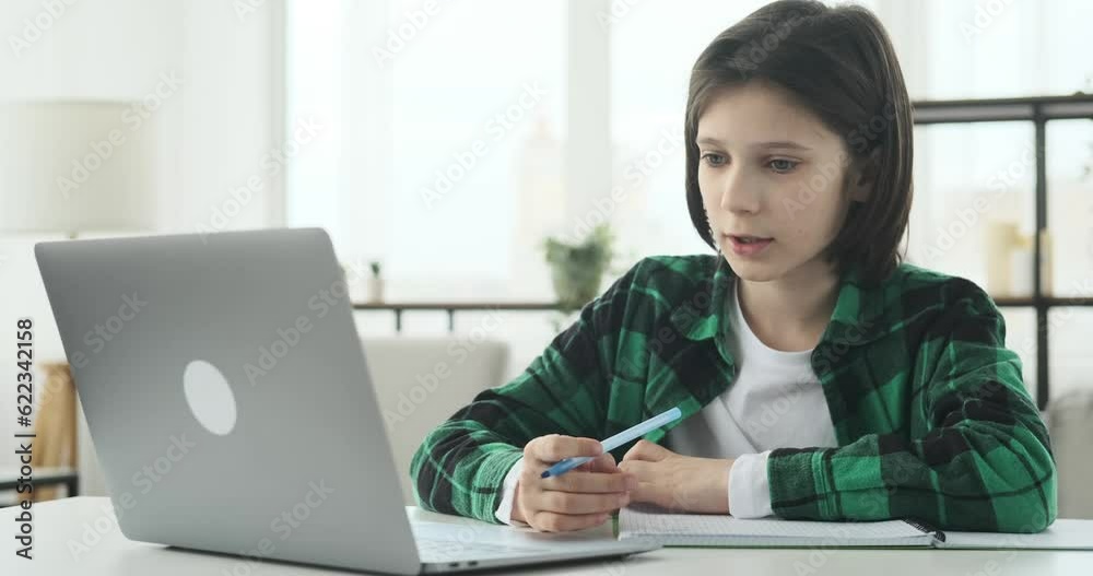Caucasian schoolboy in the living room as he engages in an online learning session. Seated at his desk, he participates in the virtual class, utilizing his laptop to interact with the teacher. Caucasian schoolboy in the living room as he engages in an online learning session. Seated at his desk, he participates in the virtual class, utilizing his laptop to interact with the teacher.