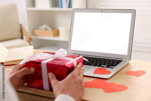 Valentine's day celebration in long distance relationship. Man holding gift box while having video chat with his girlfriend via laptop, closeup