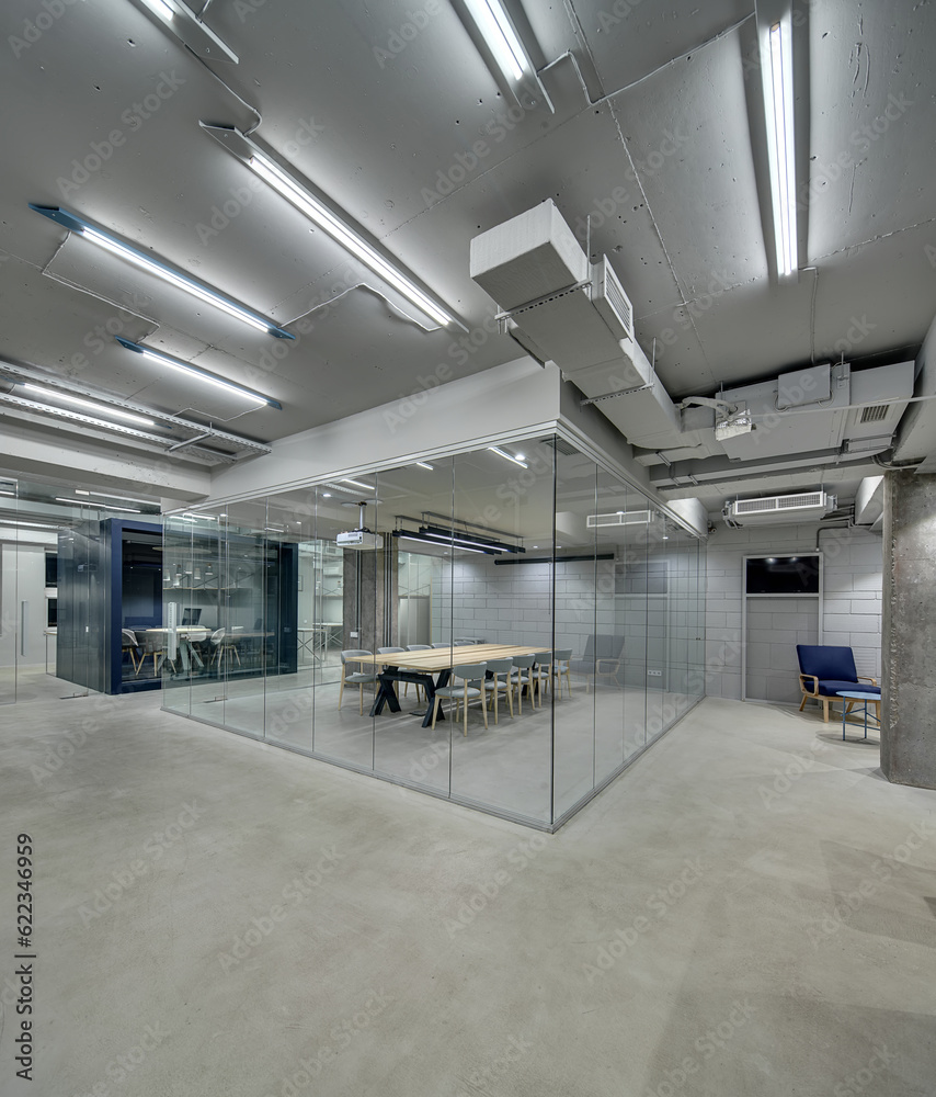 Bright office in a loft style with glowing lamps, gray brick walls and concrete columns. There are zones with furniture for meeting and conference which fenced with glass partitions. Vertical.