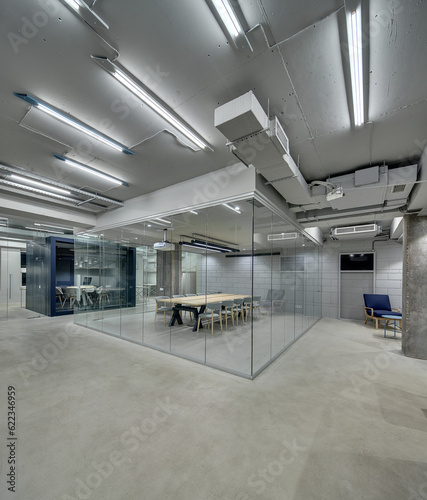 Bright office in a loft style with glowing lamps  gray brick walls and concrete columns. There are zones with furniture for meeting and conference which fenced with glass partitions. Vertical.