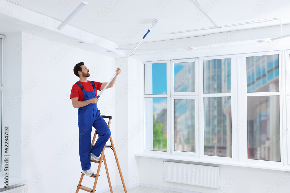 Handyman painting ceiling with roller on step ladder in room Handyman painting ceiling with roller on step ladder in room