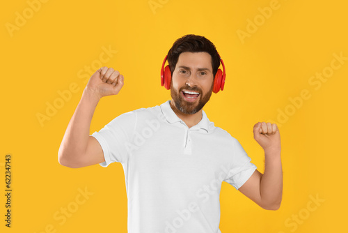 Happy man listening music with headphones on yellow background