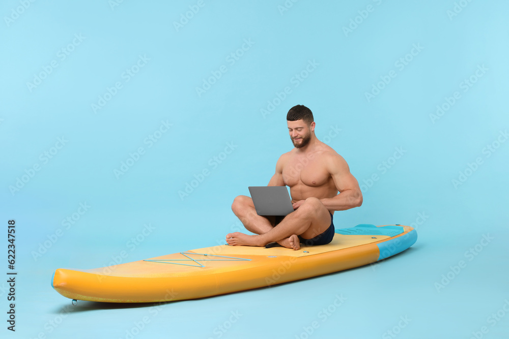 Man with laptop on SUP board against light blue background