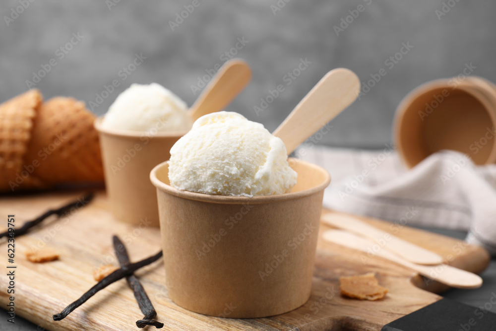 Paper cups with delicious ice cream and vanilla pods on wooden board, closeup Paper cups with delicious ice cream and vanilla pods on wooden board, closeup