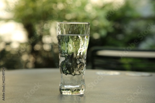 Glass of fresh water on grey table outdoors