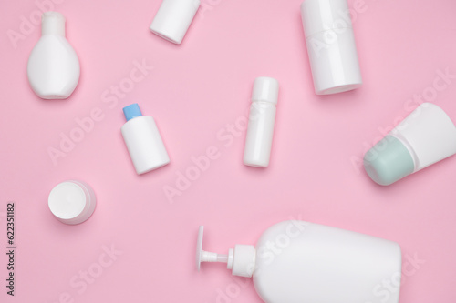 Still life. Flat lay. Various white small tester bottles with beauty products for skin and body care on pink background