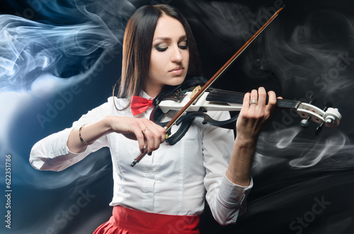 Dreamy woman playing the violin on a black background and smoke