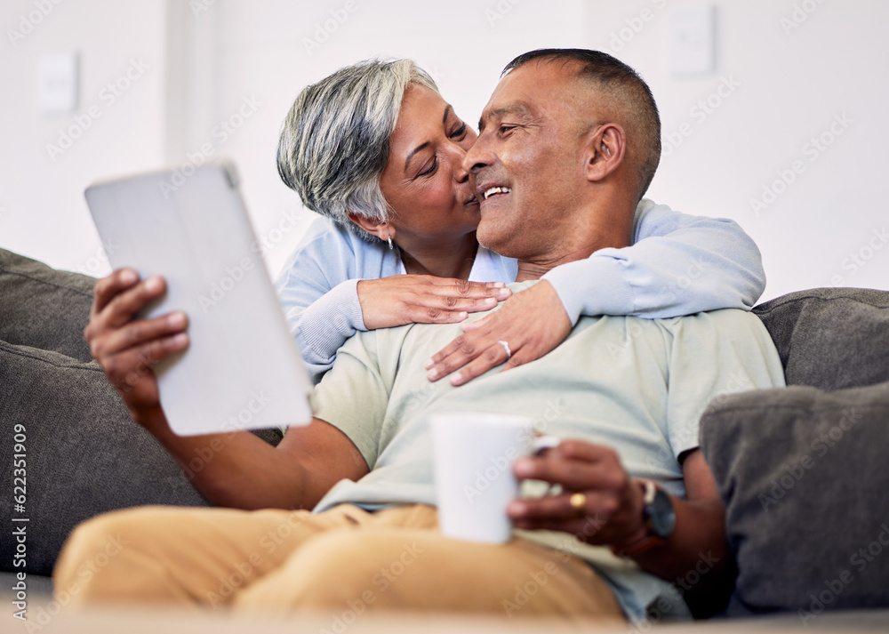 Senior couple, hug and tablet on sofa to relax with quality time in home with kiss during retirement. Couple, technology and embrace with elderly man or woman in living room together on couch. Senior couple, hug and tablet on sofa to relax with quality time in home with kiss during retirement. Couple, technology and embrace with elderly man or woman in living room together on couch.