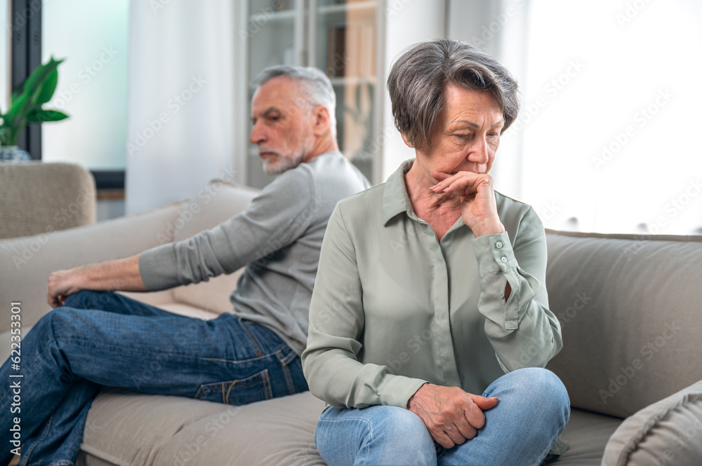 Senior couple sitting on couch and ignoring each other Senior couple sitting on couch and ignoring each other