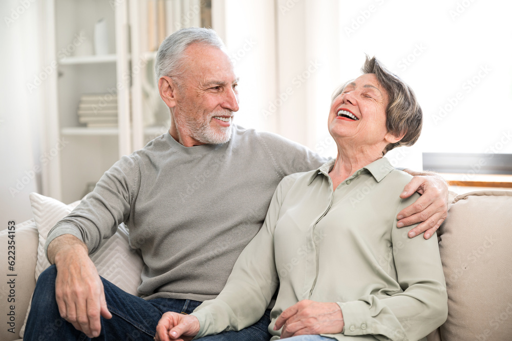 Laughing loving aged couple relaxing on cozy couch at home Laughing loving aged couple relaxing on cozy couch at home