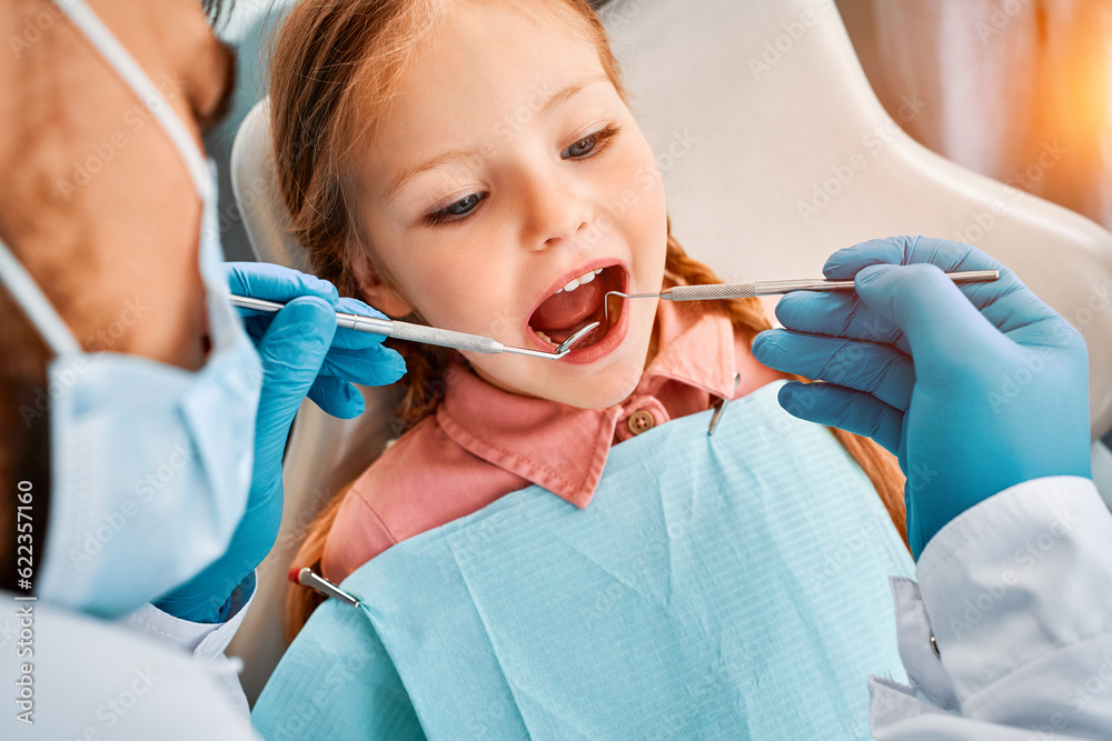 Close-up portrait of a little girl patient whose teeth are being checked by a dentist. Dental treatment, children's dentistry. Close-up portrait of a little girl patient whose teeth are being checked by a dentist. Dental treatment, children's dentistry.