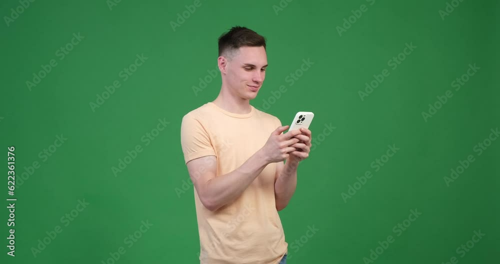 A satisfied Caucasian man is captured using his phone against a vibrant green screen background. With a contented smile on his face, he effortlessly navigates through his phone. A satisfied Caucasian man is captured using his phone against a vibrant green screen background. With a contented smile on his face, he effortlessly navigates through his phone.