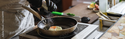 Professional kitchen worker cooking egg on a frying pan to make delicious breakfast