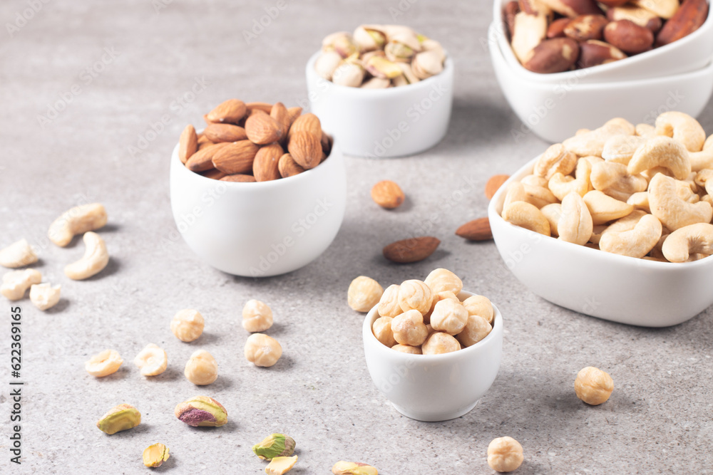 Large assortment of nuts in different bowls on stone table.