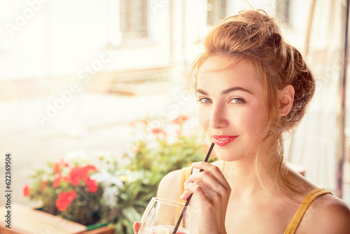 Fashion Girl Drinking Cocktail in a Cafe Terrace Outdoors. Smiling Trendy Woman in the City. Stylish Young Female. Toned Photo with Copy Space.