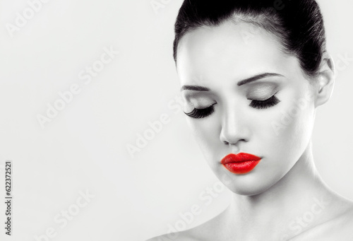 beautiful woman with dark makeup and red lipstick posing on light grey background. Black and white image. © Designpics