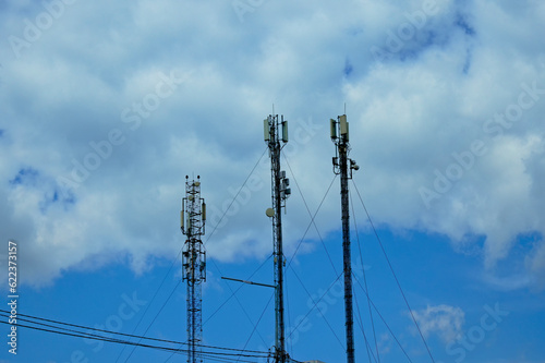 Three telecommunication towers cells for mobile communications against cloudy sky. Three base radio station. Telecommunication towers of 4G and 5G cellular. GSM transmitters. Abstract view