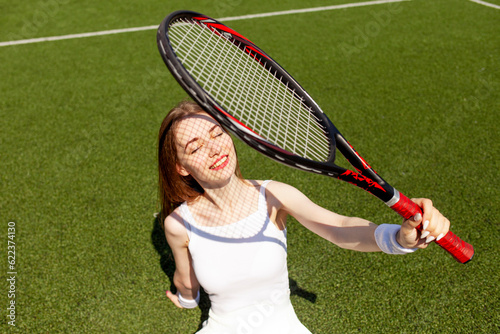 girl tennis player in white sports uniform with tennis racket sits and rests on green court, woman coach smiles