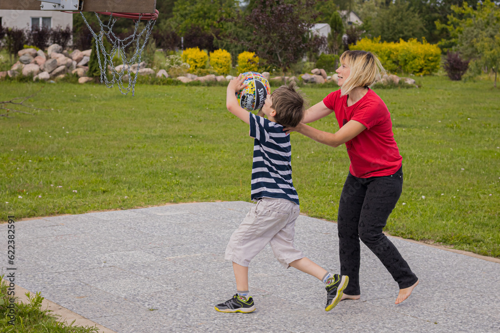 Fototapeta premium A mother plays streetball with her child. A child plays basketball with a woman