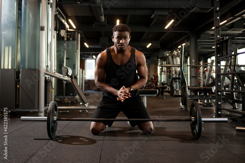 african american man lifts barbell in dark gym, sports guy trains in fitness room and goes in for sports