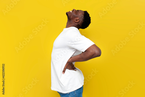 african american man in white t-shirt holding on to his back and bending over yellow isolated background