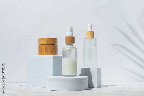 Trendy background with natural cosmetic skincare bottles. Product presentation. Beauty and body care product concept. Beauty oil and face cream in white frosted glass bottles.