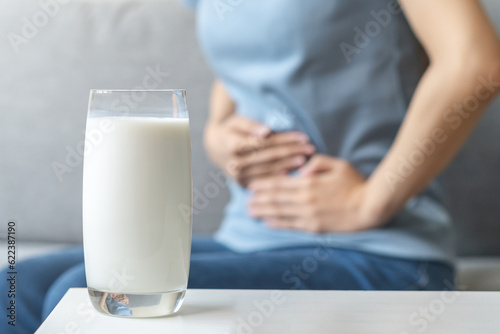 Pain, suffering asian young woman having a stomachache, abdominal pain or digestive, hand in holding belly after drink glass of milk. Lactose intolerance, allergy from dairy food, health care problem.