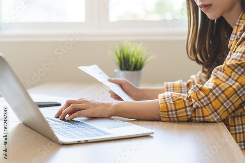 Bill pay concept. Online internet banking asian young woman work at desk on laptop computer at home  female calculate finance  hand holding paperwork  bills tax for payment. Technology of financial.