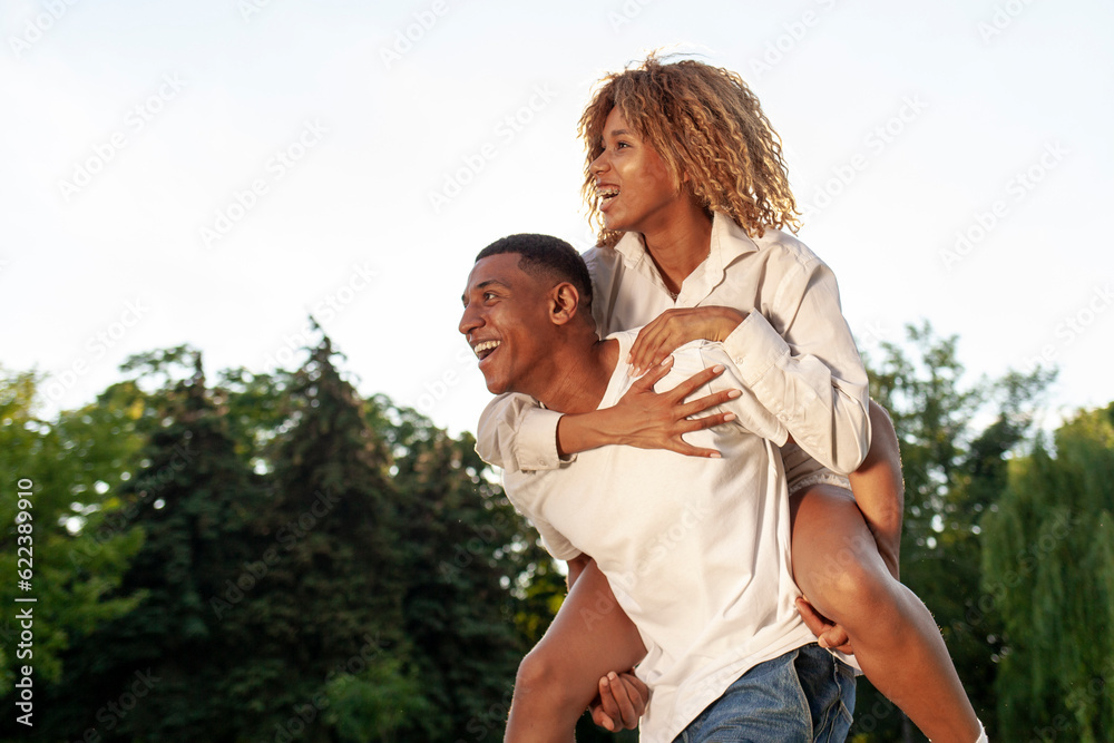 Obraz premium african american happy couple walk together in park in summer and look at copy space, man carries woman