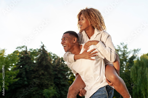 african american happy couple walk together in park in summer and look at copy space, man carries woman