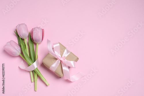 Beautiful gift box with bow and tulips on pink background  flat lay. Space for text