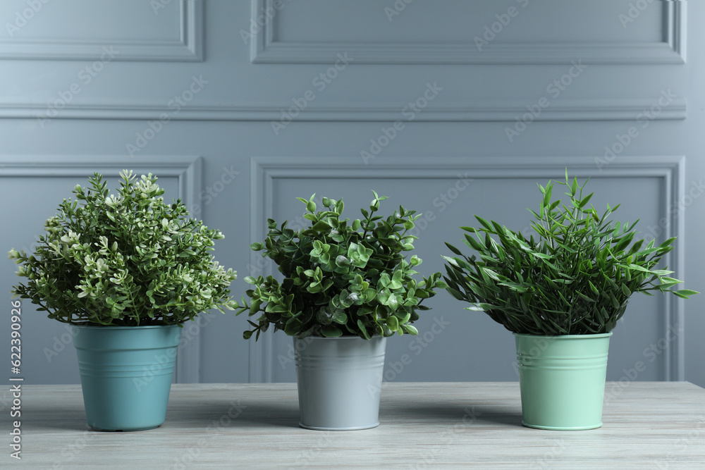 Many different artificial plants in flower pots on white wooden table near grey wall Many different artificial plants in flower pots on white wooden table near grey wall